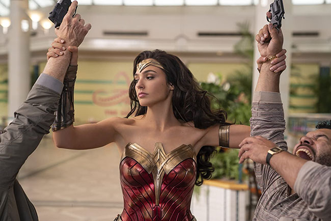 Wonder Woman apprehends two robbers, by grabbing their arms as they hold guns. WW84